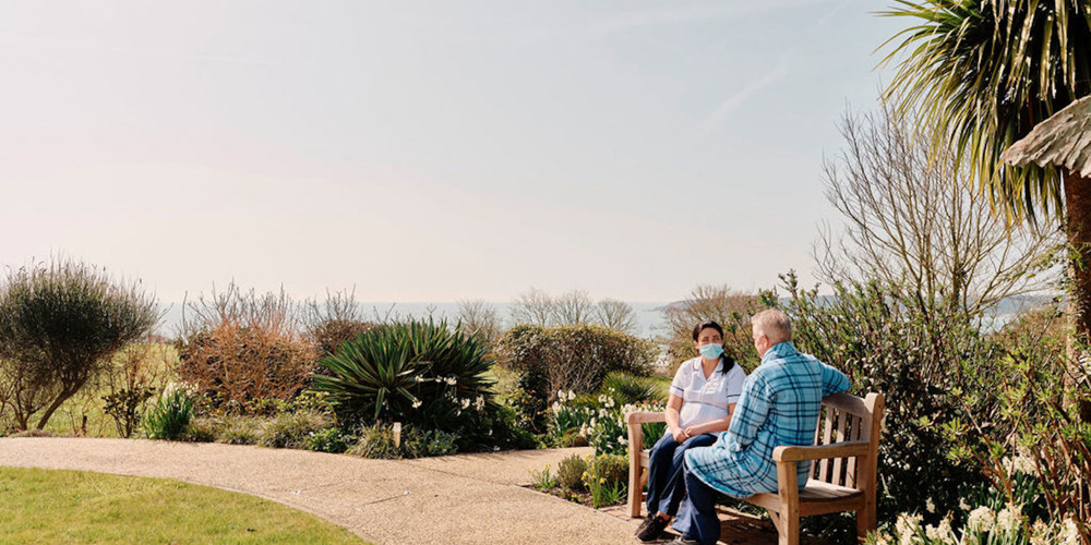 Image of nurse and patient sat on bench in Hospice gardens 
